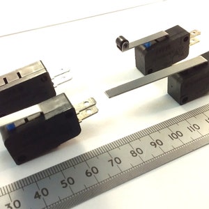 May include: A white ceramic mug with a black handle and the text "But First, Coffee" in a black, bold font. The mug is on a white surface. The mug is approximately 4 inches tall.