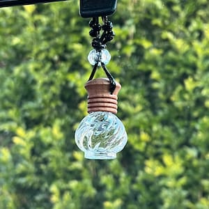 May include: A clear glass car air freshener with a wooden top and a black string hanging from a rear view mirror.