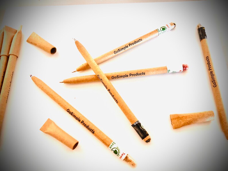 May include: A collection of eco-friendly pens and pen components made from light brown paper. The pens are scattered across a white surface, some with the text "GoSimple Products" printed on them. The image suggests a focus on sustainable office supplies.