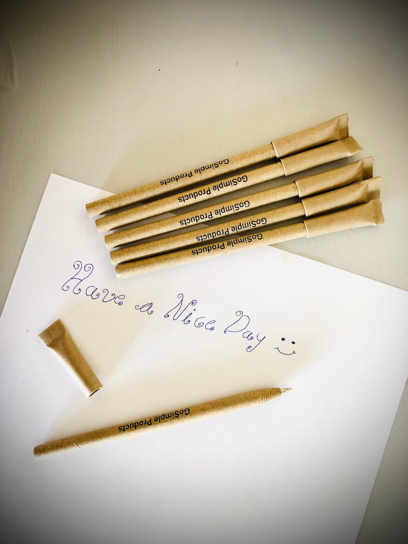 May include: A collection of beige pens with the text "GoSimple Products" printed on them, arranged on a white sheet of paper. The paper also has the handwritten phrase "Have a Nice Day" and a smiley face.