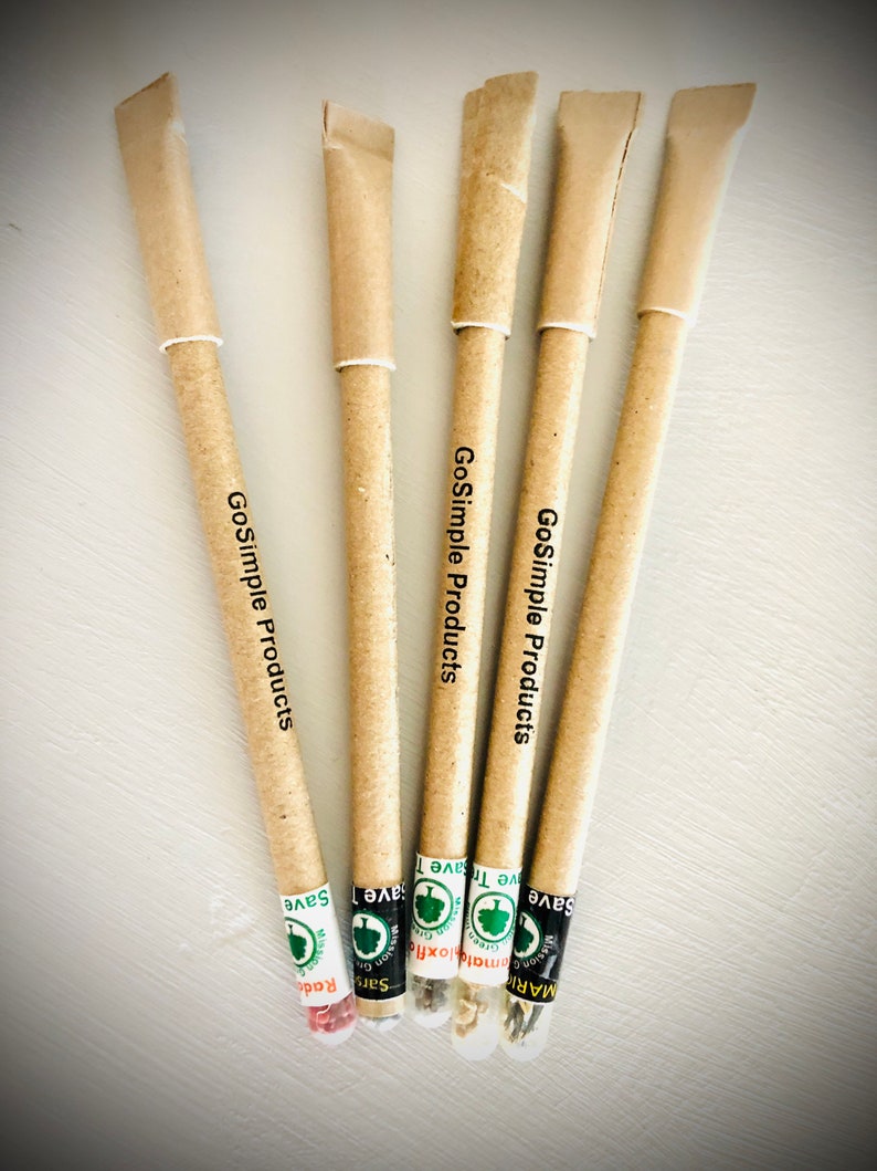 May include: Five eco-friendly pens with seed packets at the base. The pens are made of tan paper with the text "GoSimple Products" printed on them. Each pen has a different seed type, labeled with text and a green logo. The pens are arranged on a white surface.