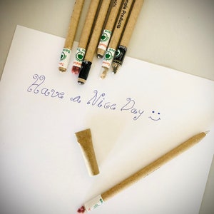 May include: A collection of eco-friendly pencils and a pen made from recycled materials, with the text "GoSimple Products" printed on them. The pencils and pen are lying on a white sheet of paper with the handwritten message "Have a Nice Day".