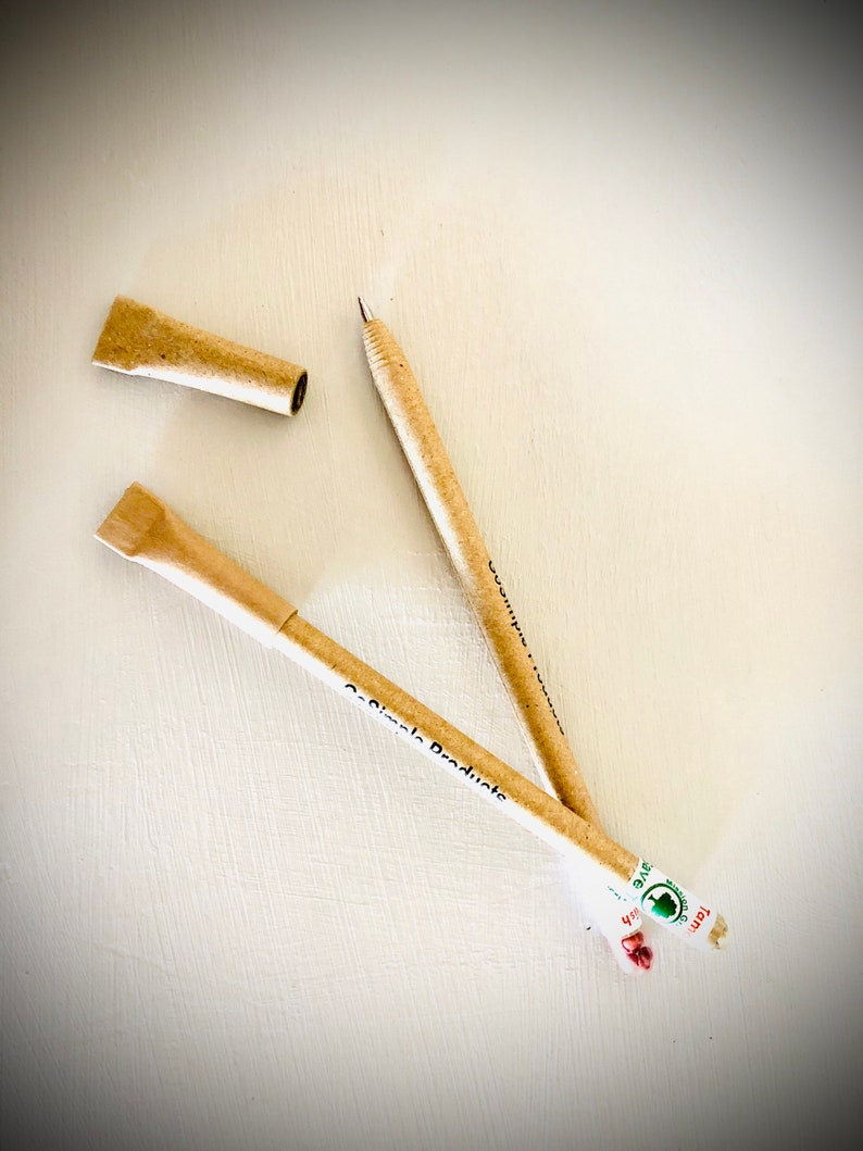 May include: Two beige pens with the text "Co-Simple Products" and a pen cap are displayed on a white surface. One pen is uncapped, revealing the writing tip. The pens are made of a light brown material, possibly recycled paper.