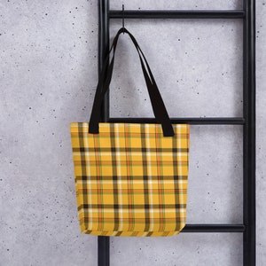 May include: Yellow and black plaid tote bag with black handles. The bag is hanging from a black metal ladder.