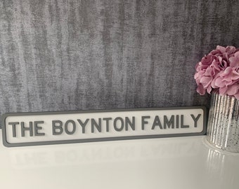 May include: A gray and white sign with the text "THE BOYNTON FAMILY" in raised letters. The sign is on a gray textured background.