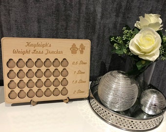 Może przedstawiać: Drewniany tracker utraty wagi z wygrawerowanym napisem "Kayleigh's Weight Loss Tracker". Tracker ma 40 małych kółek, z których każde reprezentuje 0,5 stone, oraz skalę po prawej stronie pokazującą 0,5 stone, 1 stone, 1,5 stone i 2 stone.