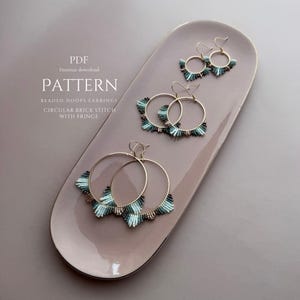 May include: A collection of beaded hoop earrings with a circular brick stitch and fringe, displayed on a light pink oval tray. The earrings feature gold hoops with turquoise and dark blue beads. The image also includes the text "PATTERN".
