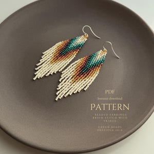 May include: A pair of beaded fringe earrings with a pattern of cream, teal, brown, and gold beads. The earrings are displayed on a brown plate. The text "PATTERN" and other details are visible.