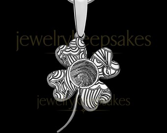 May include: A silver-toned four-leaf clover pendant suspended from a chain. The clover features intricate black etched line patterns and a central circular area displaying a detailed human fingerprint. The text jewelrykeepsakes is visible.