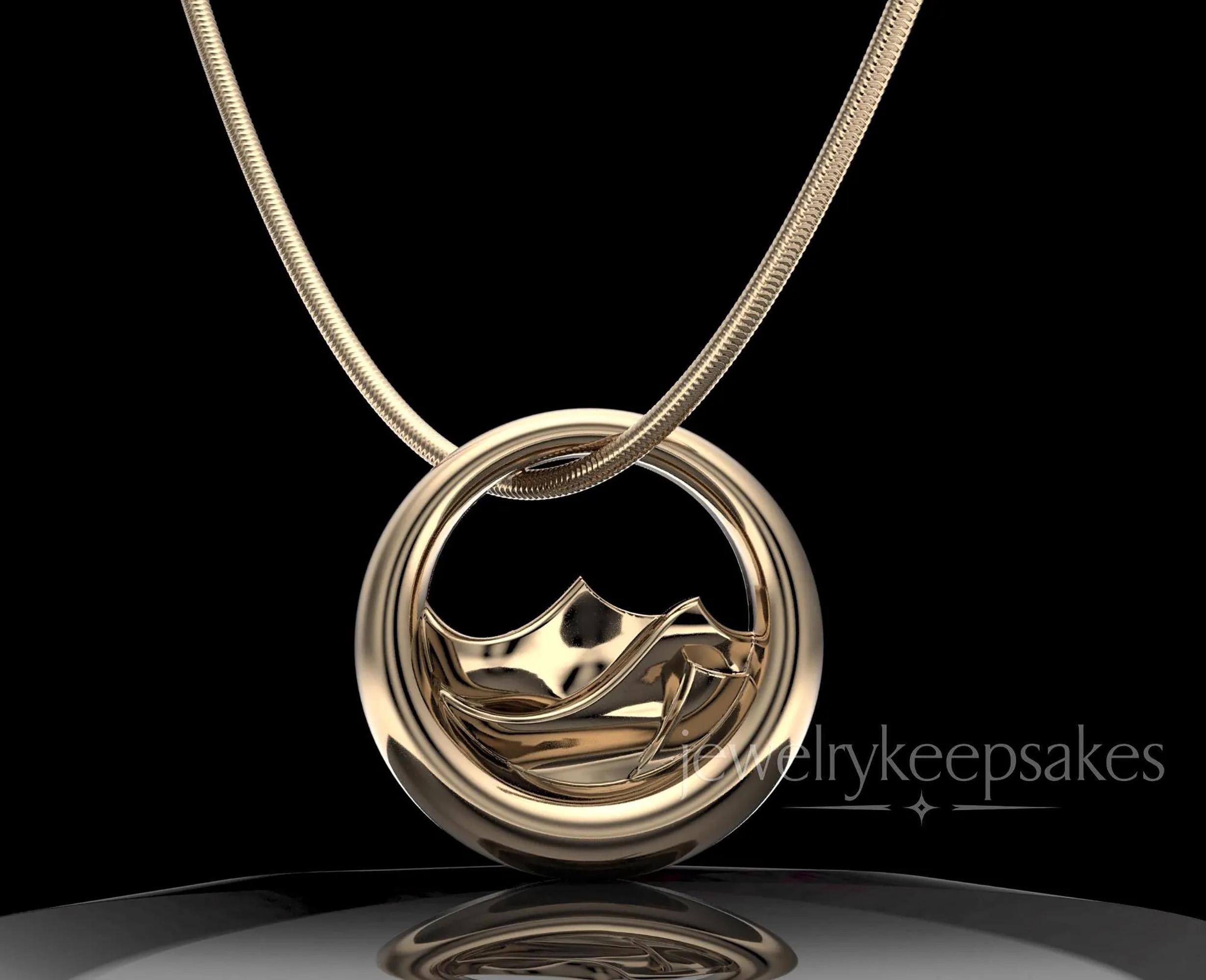 May include: A gold-toned circular pendant necklace featuring a stylized wave design within the center of the ring. The pendant hangs from a matching gold-toned snake chain. The text jewelrykeepsakes is visible in the lower right corner.