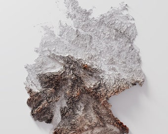May include: A 3D topographic map of Germany, showing the country's varied terrain. The map is made of a textured material, with shades of brown, white, and gray representing different elevations. The map is set against a white background.