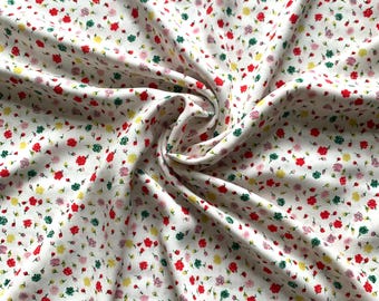 May include: White fabric with a repeating pattern of small, colorful flowers in red, pink, yellow, and green. The fabric is folded and draped, showing the texture and flow of the material. The floral design is scattered across the white background.