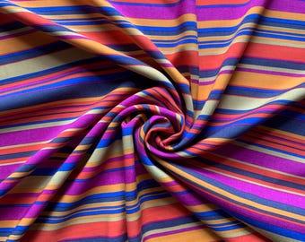 May include: A vibrant fabric with a repeating pattern of horizontal stripes in shades of purple, orange, blue, and tan. The fabric is gathered and swirled, creating a dynamic display of color and texture. The stripes vary in width, adding visual interest.