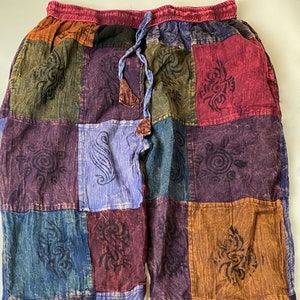 May include: Patchwork trousers with a colourful, geometric pattern. The trousers have a drawstring waist and a relaxed fit.