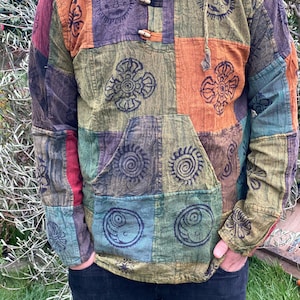 Könnte beinhalten: Ein mehrfarbiges Patchwork-Shirt mit langen Ärmeln und einer Kapuze. Das Shirt zeigt verschiedene kreisförmige und geometrische Muster in Grün-, Braun-, Orange- und Blautönen.