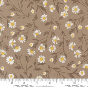May include: Tan fabric with a repeating pattern of white daisies with yellow centers and brown stems and leaves. The fabric is marked with a ruler along the bottom edge.