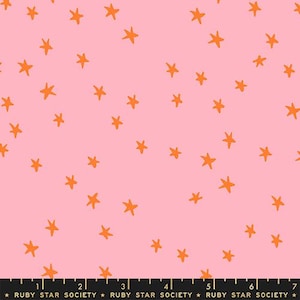 May include: Pink fabric with a scattered pattern of orange stars. The fabric has a playful, whimsical design, suitable for various craft projects. The text "RUBY STAR SOCIETY" is printed at the bottom.