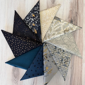 May include: A collection of triangular fabric swatches arranged in a starburst pattern. The fabrics feature various patterns, including stars, feathers, and ornate designs in shades of navy, teal, gold, and cream. The swatches are displayed on a light wood surface.