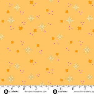 May include: A fabric with a repeating pattern of white starbursts, orange star shapes, and small purple dots on a yellow background. The fabric has a ruler along the bottom edge.