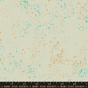 May include: A beige fabric with a speckled pattern of teal, gold, and orange dots. The fabric is marked with a ruler and the text "RUBY STAR SOCIETY".