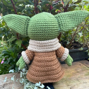 May include: A crocheted green and brown plush toy with large ears. The toy is wearing a brown coat with a cream colored collar.