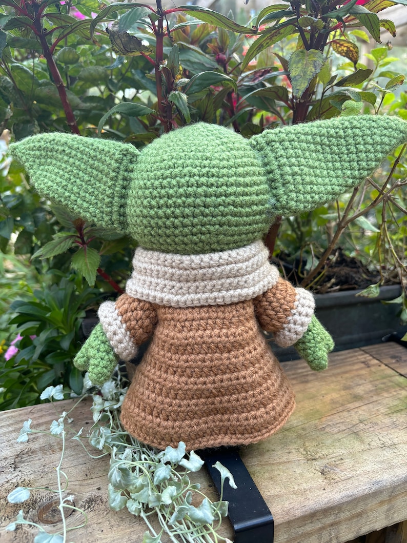 May include: A crocheted green and brown plush toy with large ears. The toy is wearing a brown coat with a cream colored collar.