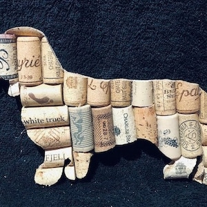 May include: A brown and white dog silhouette made from wine corks. The corks have various labels and text, including "Syrie", "white truck", "Charles Sha", and "Haut Guil".