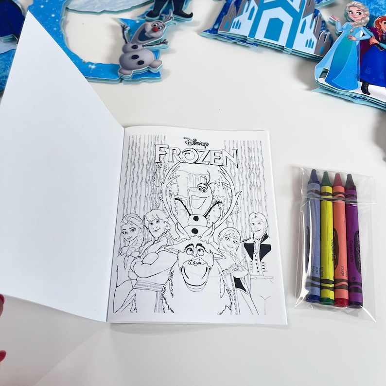 May include: A Disney Frozen coloring book featuring line art of Elsa, Anna, Kristoff, Olaf, and Sven on the cover, accompanied by a clear plastic bag containing four wax crayons in blue, yellow, red, and purple, with additional character cutouts.