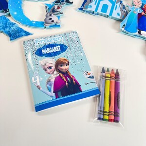 May include: A rectangular Frozen-themed coloring book featuring Elsa, Anna, and Olaf with the name MARGARET and the number 4 printed on the cover. Next to the book is a clear plastic bag containing four wax crayons in blue, yellow, red, and purple.
