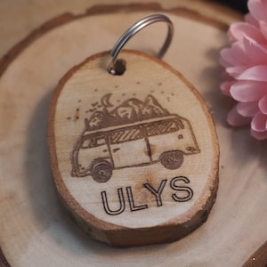 Op de afbeelding: Een houten sleutelhanger met een lasergegraveerd beeld van een vintage camper met bergen op het dak. De sleutelhanger is bevestigd aan een zilveren sleutelring en het woord "ULYS" is gegraveerd onder de camper.