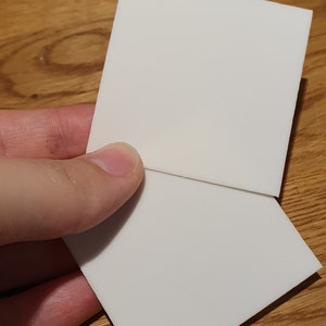 Op de afbeelding: Twee witte vierkante stukken schuimboard, in het midden bij elkaar gehouden, met een lichte hoek.