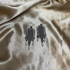 May include: A pair of silver chain earrings with pearl accents. The earrings are made of a delicate chain that hangs down from a small silver loop. The pearls are white and round, and they are attached to the chain at regular intervals.