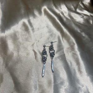 May include: A pair of silver dangle earrings with a chain link design and a long, thin, silver drop.