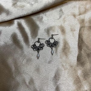 Puede incluir: Un par de pendientes de plata con un delicado diseño de cadena y una sola perla colgante en cada pendiente.