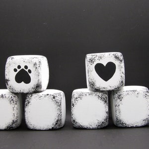 May include: Six white painted wooden blocks with black paw print and heart designs. The blocks are stacked in two groups of three. The blocks have a distressed look.