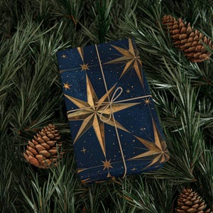 May include: A navy blue gift, patterned with gold starbursts, tied with twine. It sits on a bed of green pine needles, with pine cones scattered around. A festive, holiday-themed present.