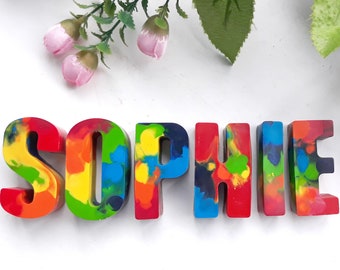 Puede incluir: El nombre "Sophie" escrito en letras de crayón de colores, multicolores. Cada letra es de un color diferente y tiene un patrón único.