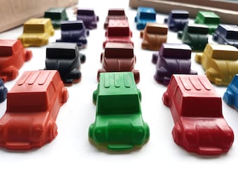 Puede incluir: Una fila de coches de juguete de colores hechos de cera, dispuestos en línea sobre una superficie blanca. Los coches son de varios colores, incluyendo rojo, verde, azul, amarillo y morado.