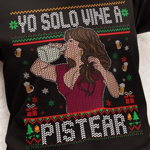 May include: Black long-sleeve sweater with a festive design. The sweater features a woman drinking from a mug, surrounded by beer mugs, snowflakes, and the text "YO SOLO VINE A PISTEAR" in white. The sweater has a red and green pattern.