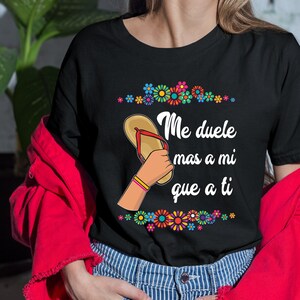 May include: Black t-shirt with a colorful graphic of a flip-flop and the text "Me duele mas a mi que a ti".