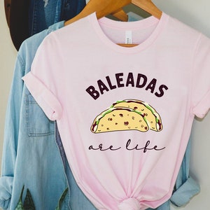 May include: Pink t-shirt with the text "BALeadas are life" and a cartoon image of two tacos.