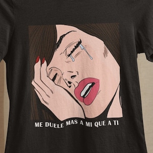 May include: Black t-shirt with a graphic of a woman with a tear rolling down her cheek. The text "ME DUELE MAS A MI QUE A TI" is printed below the graphic.