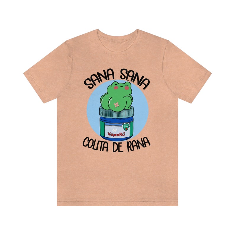 May include: A peach-colored t-shirt featuring a cartoon frog sitting on a blue and green jar of VapoR&uacute;. The text "SANA SANA COLITA DE RANA" is printed above and below the frog illustration.