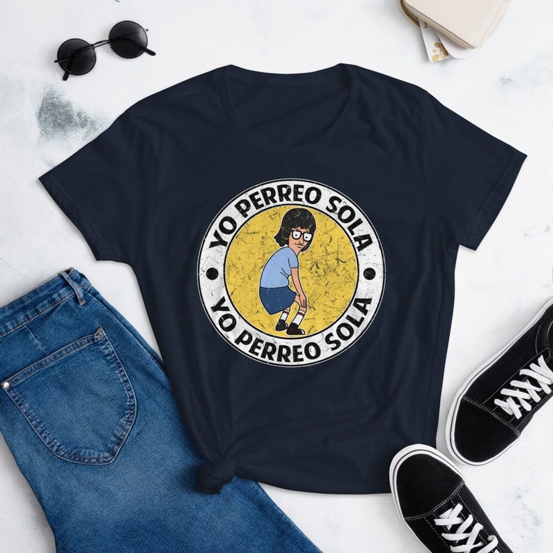 May include: A navy blue t-shirt with a white circle graphic featuring a cartoon character dancing and the text "Yo Perreo Sola" repeated twice.
