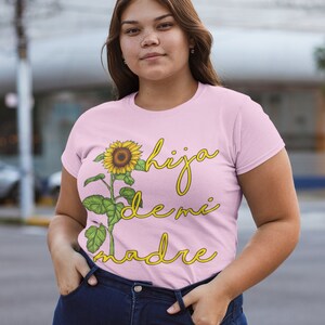 Puede incluir: Una camiseta rosa con un gr&aacute;fico de girasol y el texto "hija de mi madre" en letra amarilla.