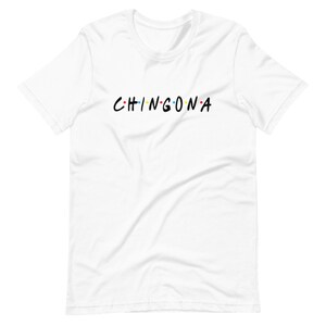 May include: White t-shirt with the text "CHINGONA" in black letters with colorful dots between each letter.