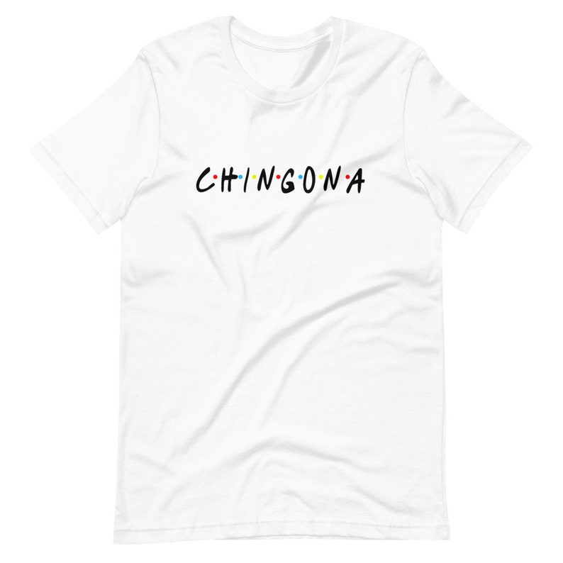 May include: White t-shirt with the text "CHINGONA" in black letters with colorful dots between each letter.