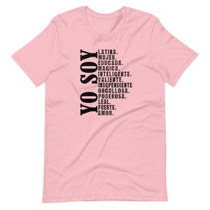 Puede incluir: Camiseta rosa con texto negro que dice "YO SOY" y una lista de palabras en espa&ntilde;ol que describen a una mujer latina, incluyendo "Latina, Mujer, Educada, Magica, Inteligente, Valiente, Independiente, Orgullosa, Poderosa, Leal, Fuerte, Amor."