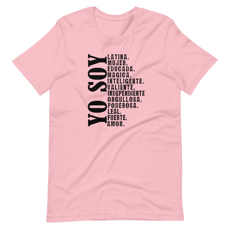 Puede incluir: Camiseta rosa con texto negro que dice "YO SOY" y una lista de palabras en espa&ntilde;ol que describen a una mujer latina, incluyendo "Latina, Mujer, Educada, Magica, Inteligente, Valiente, Independiente, Orgullosa, Poderosa, Leal, Fuerte, Amor."