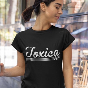 May include: Black t-shirt with white text that reads "Toxica AF" in a retro font.
